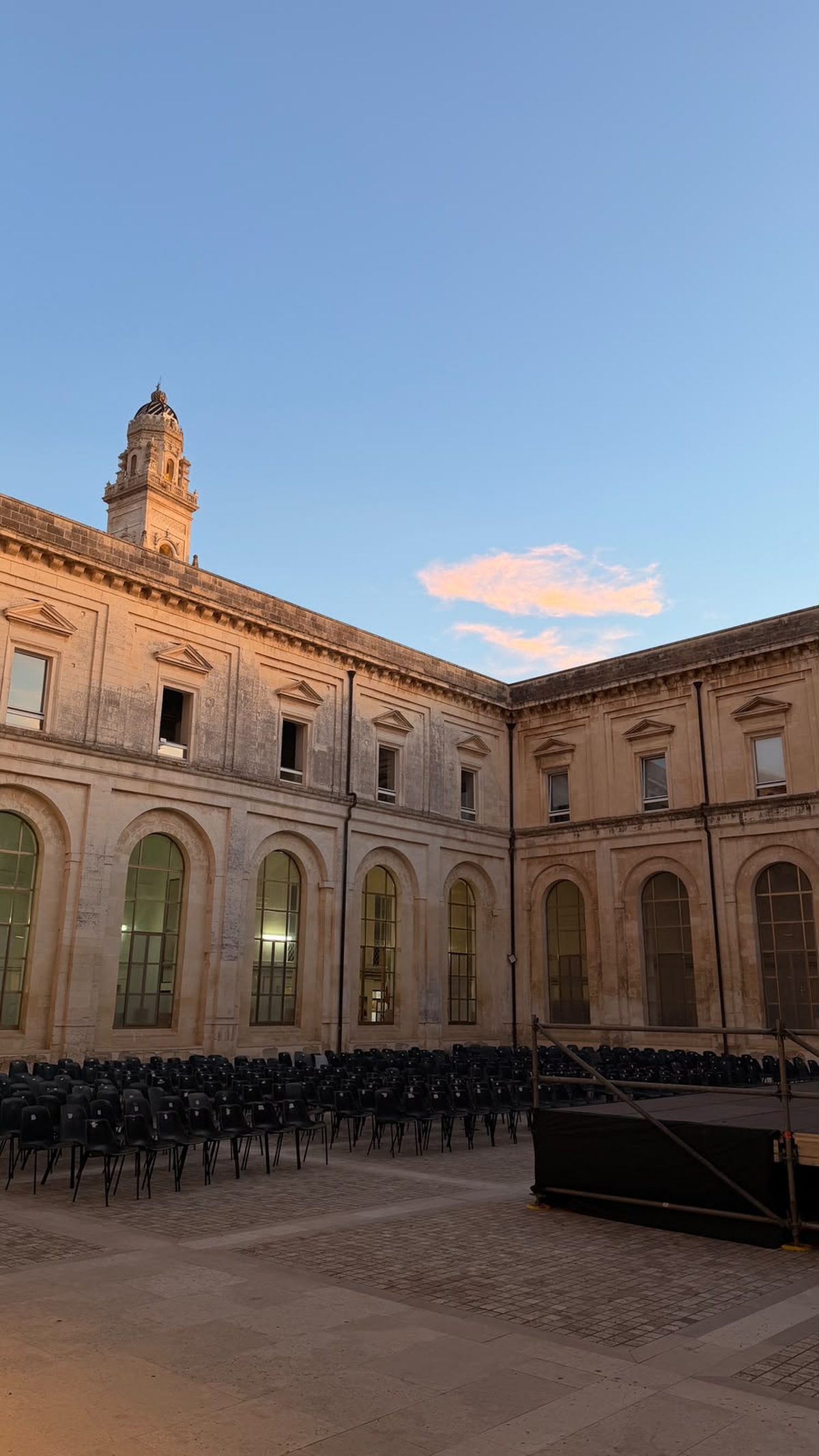 Il chiostro al tramonto con le file di sedie nere allestite e il palco montato, prima dell'inizio dello spettacolo