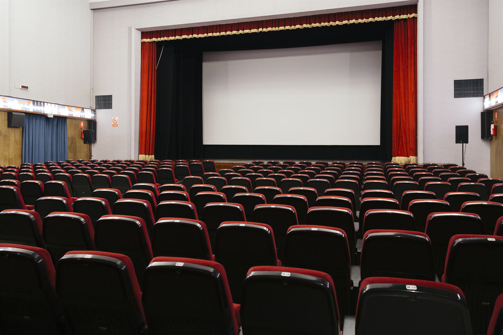 La sala vista dal fondo: file di poltrone rosse e nere rivolte verso lo schermo incorniciato dal sipario
